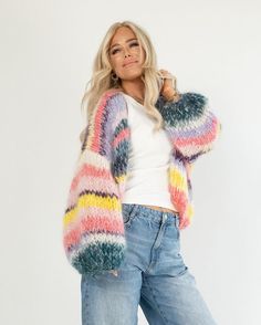 a woman is posing for the camera wearing a colorful cardigan sweater and ripped jeans