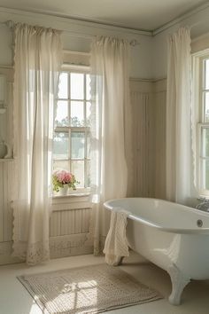 a white bath tub sitting next to a window in a room with curtains on the windowsill