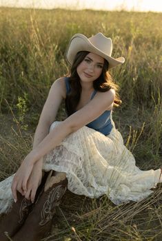 a woman sitting in the grass wearing a cowboy hat