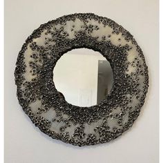 a round mirror hanging on the wall with black beads around it and a white background