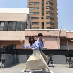 two people standing on top of a roof with their arms in the air while one person holds his hand up