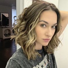 a woman with shoulder length wavy hair standing in front of a mirror and looking at the camera