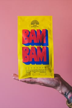 a hand holding up a yellow bag with the word bam in red and blue on it