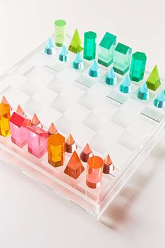 a clear plastic tray with different colored objects in it on a white surface, including one pink building and two green buildings