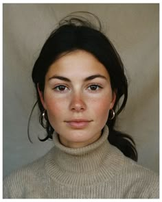 a woman with brown hair and blue eyes wearing a turtle neck sweater looking at the camera