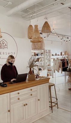 a woman sitting at a counter with a laptop in front of her and some lights hanging from the ceiling