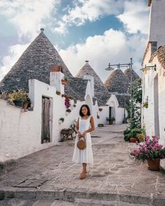 a woman is standing in an alleyway with whitewashed buildings and potted plants