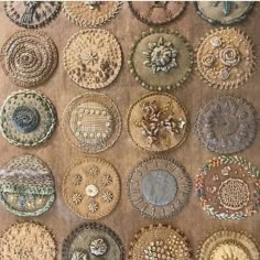 a bunch of different types of buttons on a piece of brown fabric with gold thread