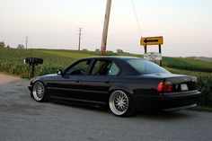 a black car parked on the side of a road next to a corn field and telephone pole