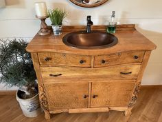 a bathroom sink sitting on top of a wooden counter next to a mirror and potted plant