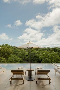 two lounge chairs sitting under an umbrella on top of a patio next to a swimming pool