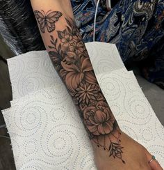 a woman's arm with flowers and butterfly tattoo on her left arm, sitting on a table