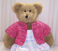 a brown teddy bear wearing a pink jacket and white dress sitting on a chair in front of a striped wall