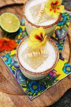 two glasses filled with drinks on top of a wooden tray next to sliced limes