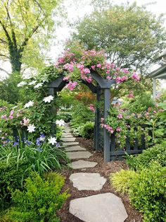 a garden with lots of flowers on the side of it and a stone path leading to an arbor