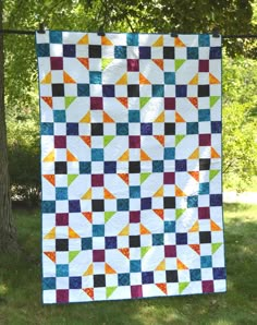 a colorful quilt hanging on the side of a tree in front of a green field