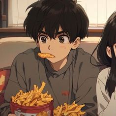 two people sitting on a couch eating french fries in front of a bowl of chips