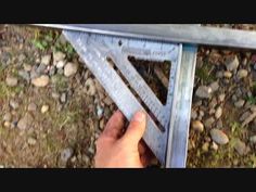 a person is holding a metal ruler over some rocks and grass with their hand on the ground