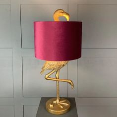 a gold flamingo lamp with a pink shade on it's head and legs