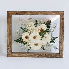 a wooden frame with flowers and greenery in it on a white wall next to a candle