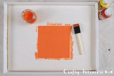 an orange square with some paint and a brush sitting on the table next to it