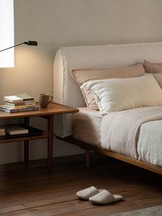 a bed with pillows and blankets on it next to a night stand, lamp and book