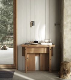 a wooden table sitting in front of a glass door next to a tree stump on the floor