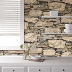 a stone wall with shelves and dishes on the shelf next to it, in front of a window