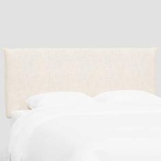 a bed with white linens and pillows on top of the headboard, in front of a gray wall