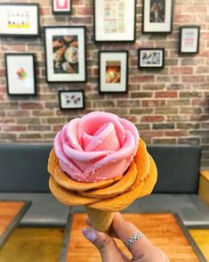 a hand holding an ice cream cone with pink frosting on it in front of a brick wall