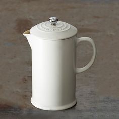 a white ceramic tea pot with a lid and handle on a concrete surface, in front of a wall