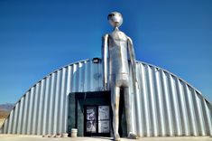 a large metal statue stands in front of a building with an open door on the side