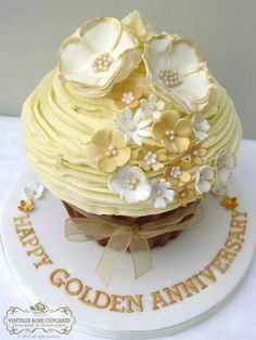 a cupcake decorated with flowers on top of a white cake plate that says happy golden anniversary