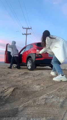 a person sitting on the hood of a car looking out at an ocean and sunset