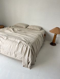 an unmade bed sitting in a bedroom next to a table with a lamp on it