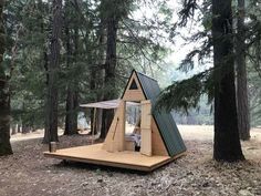 a small wooden cabin in the woods surrounded by pine trees with a sleeping area inside