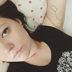 a woman laying on top of a bed next to a white pillow covered in tattoos