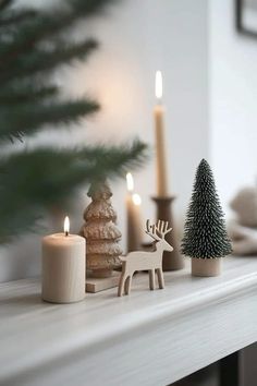 christmas decorations on a mantle with candles and trees in the foreground, against a white wall