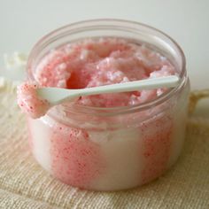 a jar filled with pink jello sitting on top of a wooden table next to a spoon