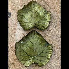 two green leaf shaped plates sitting on top of a tile floor