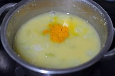 a silver pot filled with yellow liquid on top of a stove burner and topped with an orange substance