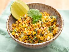 a bowl filled with corn, cilantro and lime next to a lime wedge