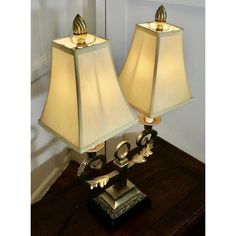 two lamps sitting on top of a wooden table next to each other, one is gold and the other is white