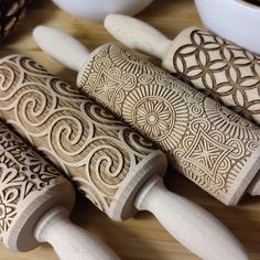 four carved wooden spoons sitting on top of a table next to bowls and pine cones