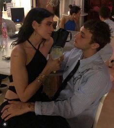 a man and woman sitting next to each other at a table with drinks in front of them