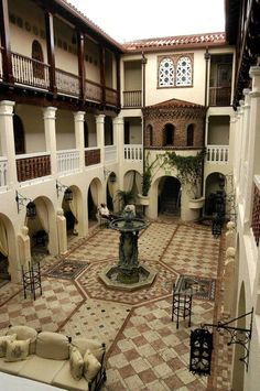 an indoor courtyard with fountain, seating and potted plant in the center on tiled flooring