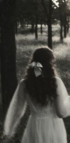 a woman in a white dress walking through the woods with her hands behind her back