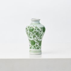 a green and white vase sitting on top of a table next to a wall in the background