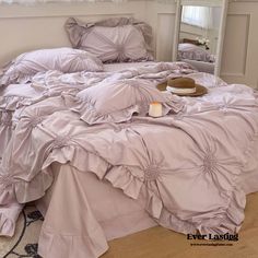 an unmade bed with ruffled sheets and pillows on the floor next to a mirror