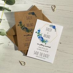 three wedding cards with blue flowers on them sitting next to each other and greenery in the background